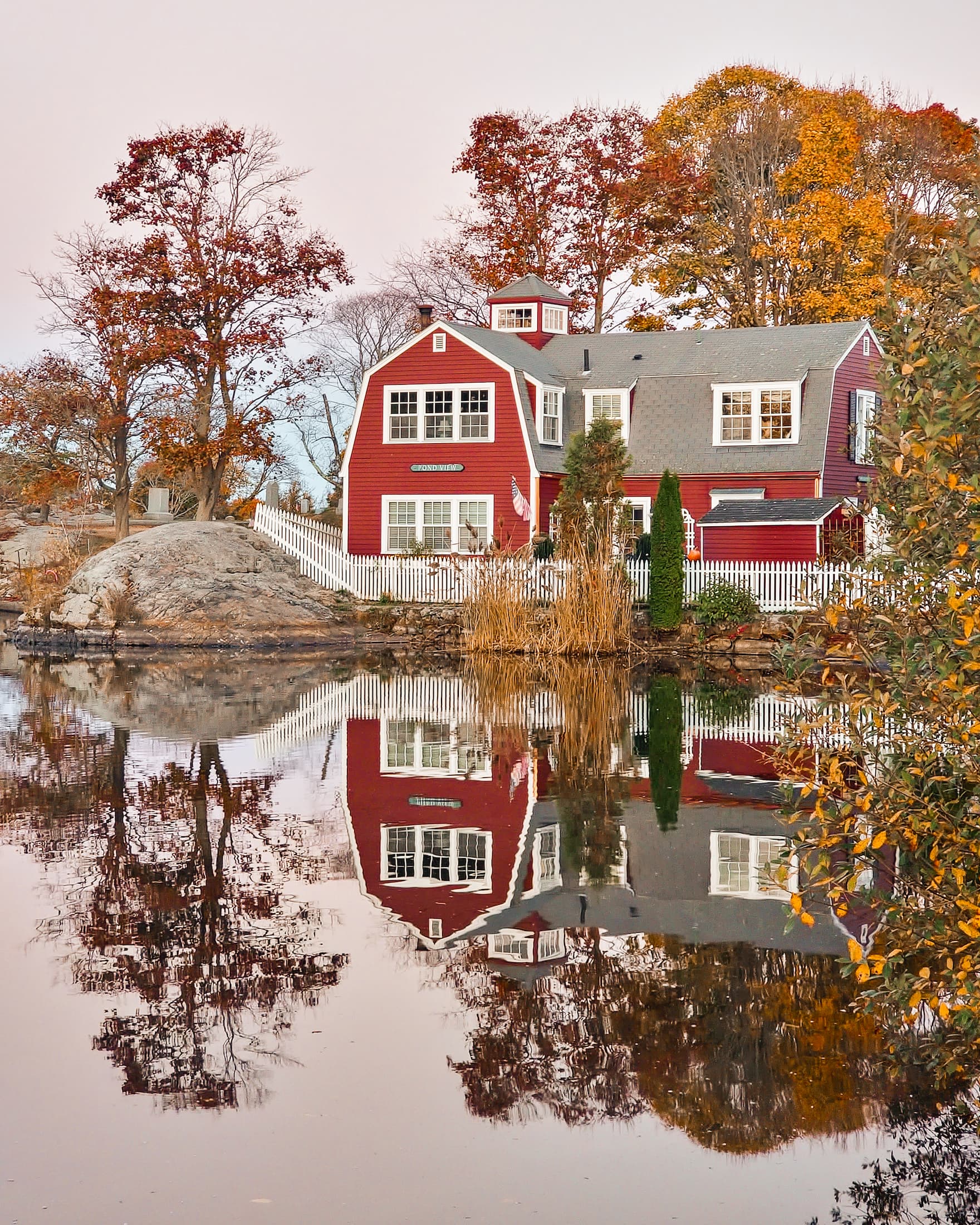 Red colonial farmhouse reflected in a Marblehead pond in autumn